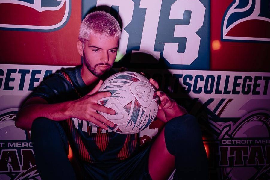A young man holds a football under dim red lighting